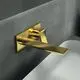 Wandarmatur aus gebürstetem Gold von Ideal Standard, mit eckiger Rosette und schwenkbarem Auslauf, montiert an einer grauen Wandoberfläche.